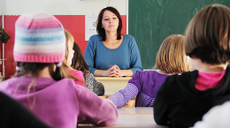 photo of teacher sitting in the front of a class of students.